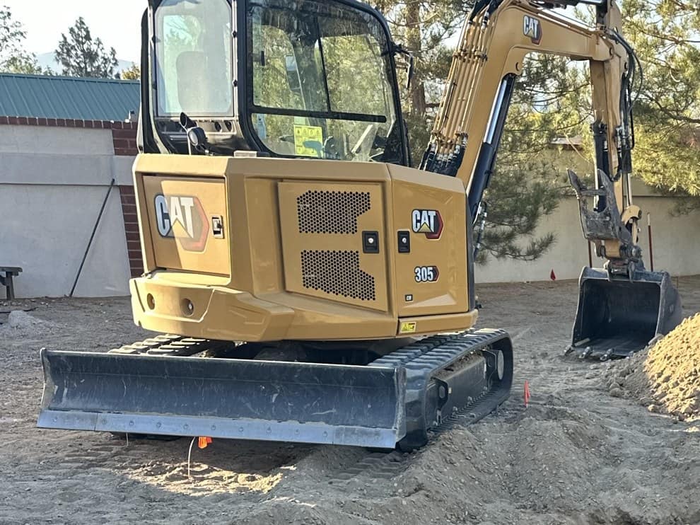 CAT mini excavator beside a freshly installed black septic tank with blue PVC plumbing
