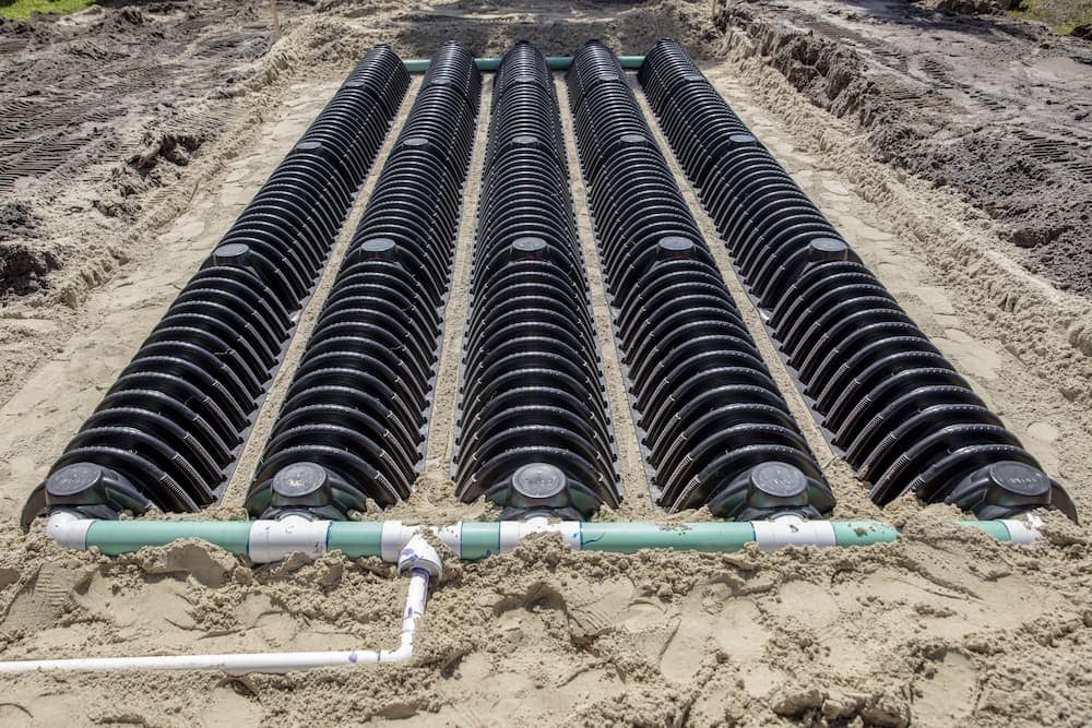 New leach field installation with rows of infiltrator chambers and green distribution pipes in sand